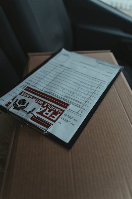 A clear view of a florist's delivery package showing a delivery note and parcel label, resting on top of a cardboard box inside a vehicle. The delivery note includes handwritten details and the parcel
